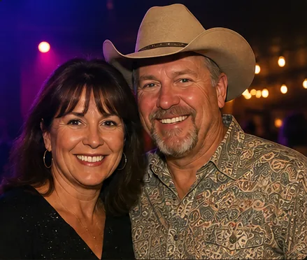 Smiling couple, one in a tan cowboy hat and western shirt, enjoying a night of live country music
